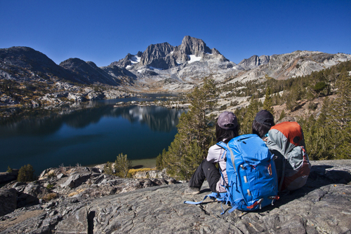 Two girls with backpacks sitting on top of hill, looking at a lake Thousand islands lakes, Eastern Sierra, California