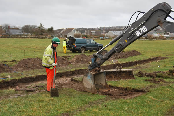 Man in high-vis with shovel stands next to digger